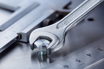 Wrench tightens bolt in steel billet. Spanner, bolt, screw and nuts.