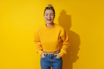Young cheerful girl wearing yellow sweatshirt and sunglasses against yellow background