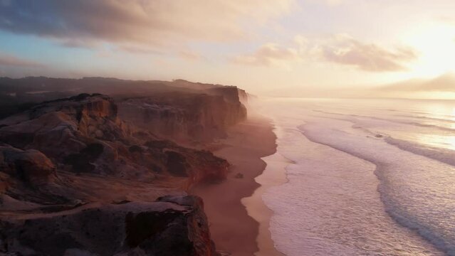 Aerial shot of end of the world cliffs near ocean beach in Portugal. Land meets water, nature elements during amazing sunrise sunlight. Dreamy pink scenery and landscape of Atlantic Ocean