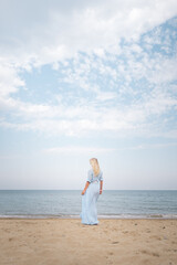 Fototapeta na wymiar sea, sky, clouds, sunset, ocean, blonde woman in a floating dress stands with her back to the viewer, blue, without face, horizontal, photo