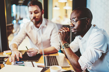 Pensive black man thinking at laptop working at table with colleagues
