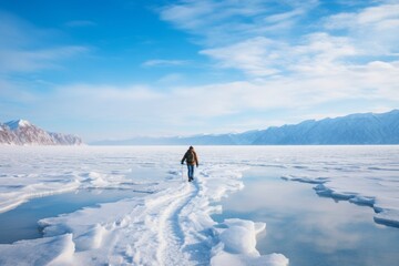solo traveler walking over frozen lake discovering the winter landscape  rear view of man standing looking at snow covered frozen mountain wilderness - obrazy, fototapety, plakaty