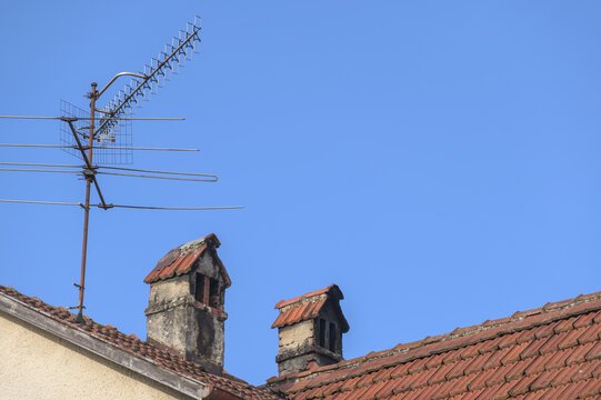 Verwitterte Kamine mit Fernseh-Antenne auf Ziegeldach vor blauem Himmel