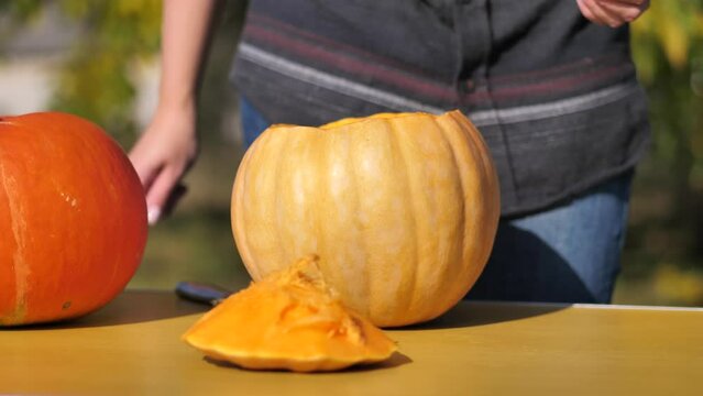 the woman cuts off the top of the pumpkin and puts it on the table. prepares a pumpkin for Halloween