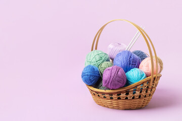 Lots of colorful knitting balls in a basket with knitting needles on a pastel purple background. Set for the hobby of knitting warm clothes or toys. Concept needlework