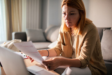 Stressed young woman going over bills and payments on the couch at home