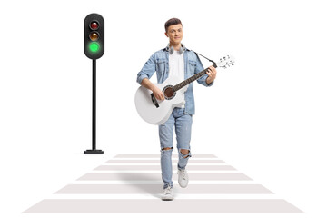 Young male playing an acoustic guitar and crossing a street at a pedestrian crosswalk