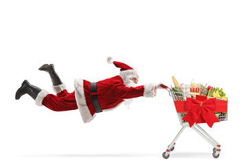 Santa claus flaying and holding a shopping cart with food and red ribbon
