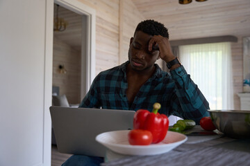 Curly-haired man sits with a laptop in the kitchen