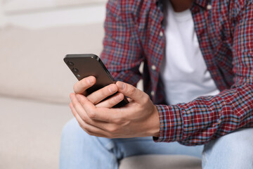 Man sending message via smartphone on sofa indoors, closeup