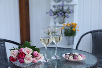Bouquet of roses, glasses with wine and candies on glass table on outdoor terrace