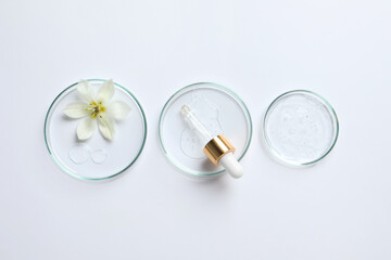 Petri dishes with samples of cosmetic oil, pipette and beautiful flower on white background, flat lay