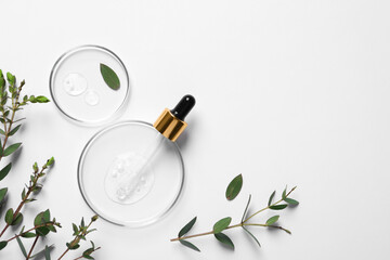 Petri dishes with samples of cosmetic oil, pipette and green leaves on white background, flat lay....