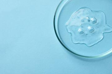 Petri dish with sample of cosmetic oil on light blue background, above view. Space for text
