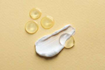 Samples of transparent gel and white cream on yellow background, flat lay