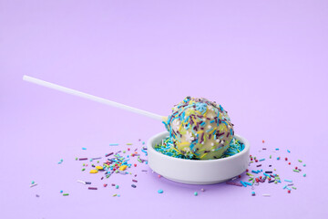 Delicious confectionery. Sweet cake pop and sprinkles on light violet background