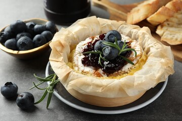 Tasty baked brie cheese with blueberries, jam and rosemary on grey table, closeup