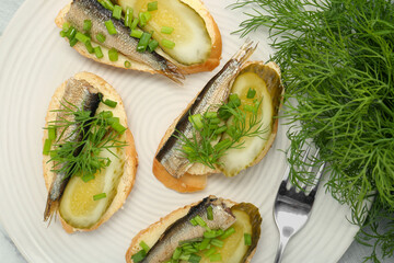 Delicious sandwiches with sprats, pickled cucumber, green onion and dill on plate, top view