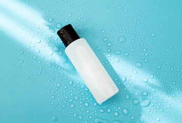 Bottle for beauty product on blue background with hard light and water drops. with shadows flat...