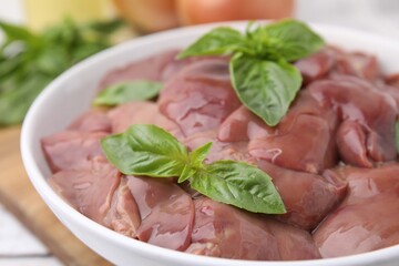 Bowl with raw chicken liver and basil on table, closeup