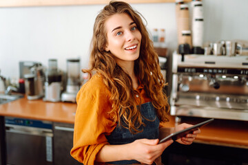 Female barista takes an order from a tablet while standing behind the counter in a coffee shop. Business, technology concept. Takeaway food.