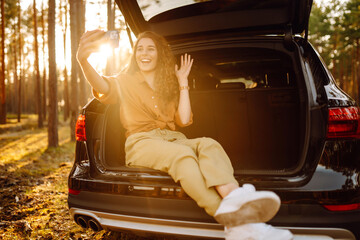 Stylish woman takes a selfie, communicates via video call from a smartphone in the trunk of a car...
