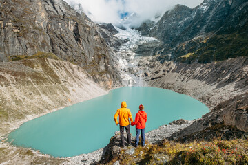 Trekkers couple dressed bright jwaterproof ackets stan on rock enjoying glacier falling in high...