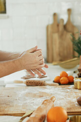 Man making christmas gingerbread cookies in modern white kitchen close up. Hands kneading gingerbread dough with rolling pin, golden metal cutters, cooking spices, festive decorations