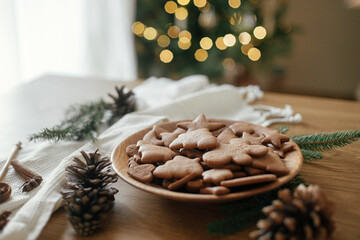 Delicious gingerbread cookies in wooden plate on rustic table against stylish christmas tree lights bokeh. Fresh baked christmas gingerbread cookies, atmospheric holiday time