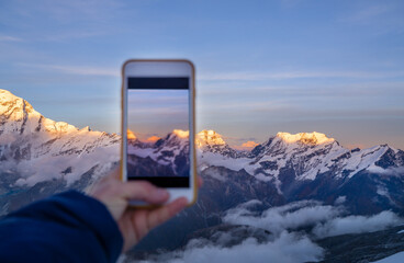 Young woman taking a vertical photo the third world's highest mountain Kangchenjunga 8586m during sunset time from the Mera Peak high camp. Climbing expedition acclimatization. Active people concept.