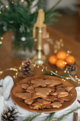 Fototapeta na wymiar Christmas gingerbread cookies in wooden plate on rustic table with fir branches, pinecone, napkin. Merry Christmas! Delicious fresh gingerbread cookies close up, atmospheric holiday