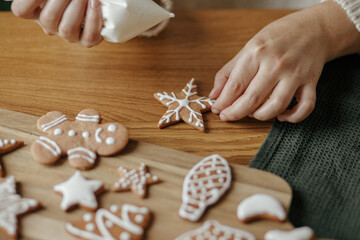 Hands decorating christmas gingerbread cookies with icing on rustic wooden table top view....