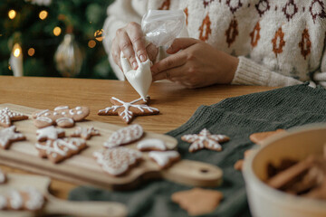 Hands decorating christmas gingerbread cookies with icing on rustic wooden table close up....