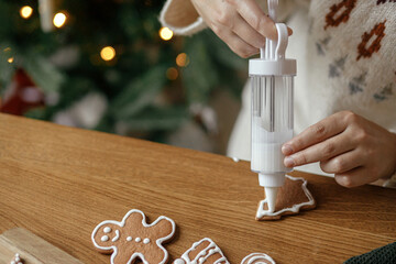 Hands decorating gingerbread cookies with icing on rustic wooden table on background of christmas...