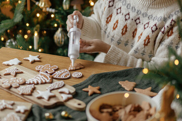 Hands decorating gingerbread cookies with icing on rustic wooden table on background of christmas...