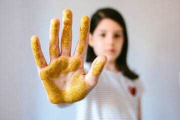 Serious young girl showing her palm hand covered of golden glitter while doing stop sign. Concept...