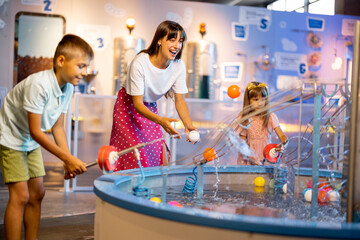 Mom with kids play with balls, learning physical phenomena in an interesting way, having fun in a science museum with interactive models - 662938149