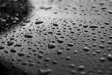 Rain or water drops different size on a black shiny car hood surface. Water droplets on dark iron surface and texture. Abstract background and water texture for design.