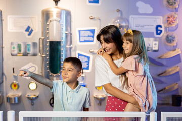 Portrait of a happy mom with her young kids visiting together a science museum. Concept of children's education and entertainment - obrazy, fototapety, plakaty