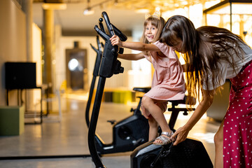 Fototapeta na wymiar Little girl with mom training on bicycle simulator, visiting science museum. Concept of children's education and entertainment