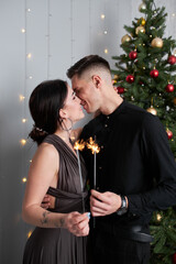 pretty couple in love kissing in christmas eve near tree with gifts at home in december.