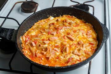 Shakshuka with tomatoes sprinkled with cheese in a frying pan on the stove.