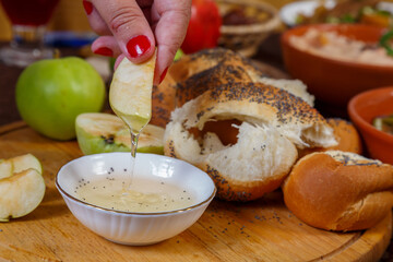 A woman's hand dips an apple in honey at the table on the Jewish holiday Rosh Hashanah.