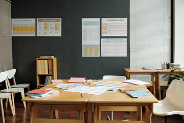 Nobody in spacious classroom of English language with documents and copybooks on wooden desk standing against wall with grammar tables