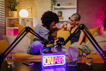Two diverse women laughing while recording episode of internet podcast