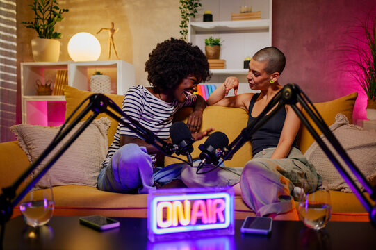 Two diverse women laughing while recording episode of internet podcast