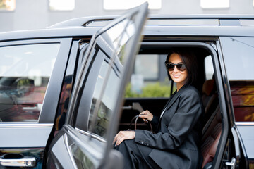 Portrait of an elegant business lady in black getting out of a luxury SUV taxi. Concept of business...