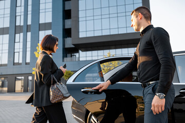 Chauffeur helps an elegant business woman gets in car, opening door of a premium taxi near office...