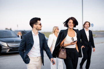 Group of an elegant business people talk on the go on parking lot, arrived by business class taxis....