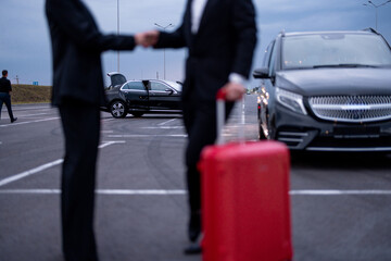 Business couple shaking hands each other while standing with a suitcase on parking lot. Concept of transportation and business trips